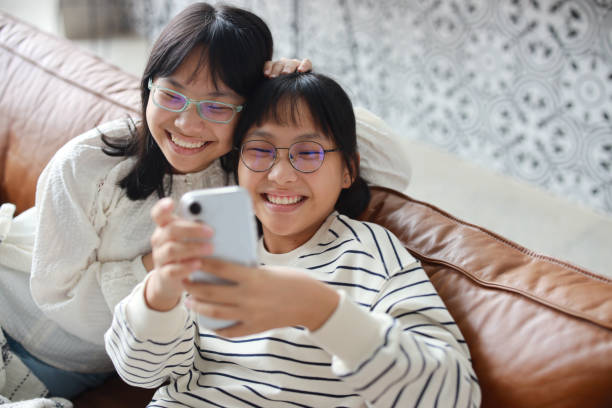 милые молодые азиатские девушки развлекаются во время видеозвонков своим друзьям с помощью смартфона, оставаясь на связи со своими близки� - having ones say стоковые фото и изображения