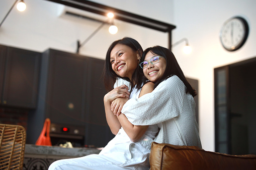 A young Asian girl is enjoying a moment of relaxation with her mother at home, symbolizing the essence of family bonding, lifestyle, and the concept of love and care.