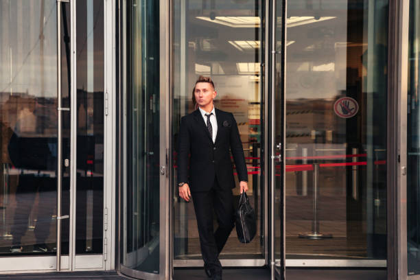 Confident young man businessman with briefcase exiting entrance business building corporate company, pensive looking away. Male walks out from office located in financial district. Copy ad text space joven hombre de negocios seguro de sí mismo con maletín que sale de la entrada de la empresa corporativa de construcción de negocios, pensativo mirando hacia otro lado. hombre sale de la oficina ubicada en el distrito financiero. copiar el espacio de te