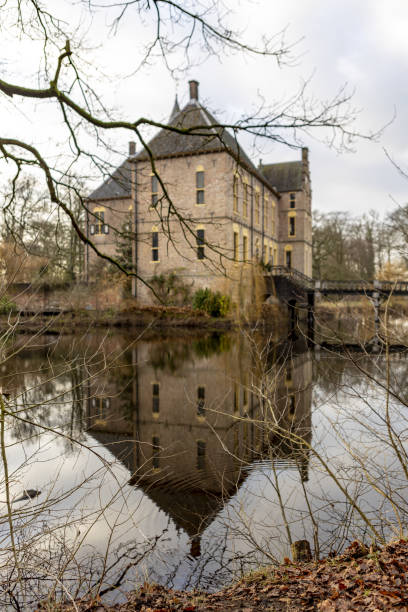 Vord, Netherlands – January 08, 2021: Mirror reflection in the water around the moated Vorden castle in winter barren branches of trees on the shore