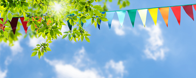 Colorida decoración de cuerdas de banderín en follaje de árbol verde en cielo azul, banner de plantilla de fondo de fiesta de verano con espacio de copia photo