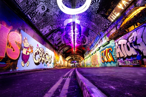 london, United Kingdom – October 31, 2022: A long tunnel with vibrant graffiti covering its walls illuminated by purple led lights