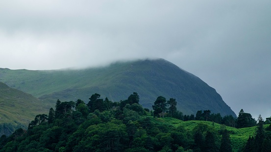 A landscape shot of lush green hills covered in trees under the cloudy sky
