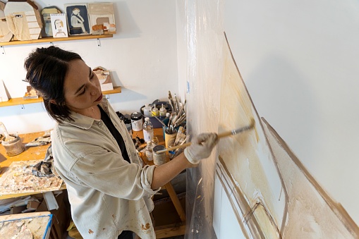 A female artist wearing protective painting gloves is focused on creating her masterpiece on a large canvas