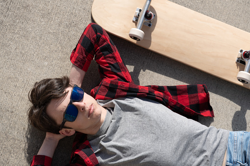 Top view of teenager skater boy lying on floor beside skateboard.