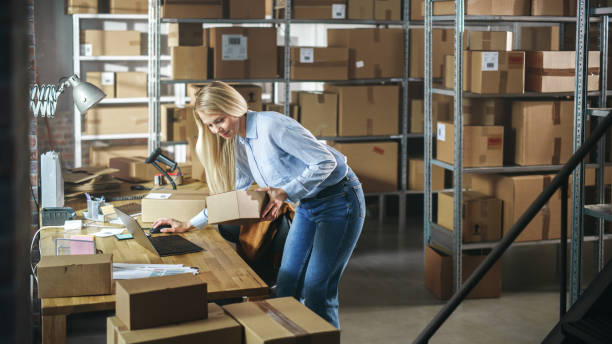 istock Inventory Storeroom Worker Comes Over to a Desk with Laptop Computer in Order to Check a Parcel Before Sending It Away. Female Working in Logistics Warehouse, Distribution Center 1478424459