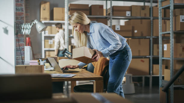 istock Inventory Storeroom Worker Comes Over to a Desk with Laptop Computer in Order to Check a Parcel Before Sending It Away. Female Working in Logistics Warehouse, Distribution Center with Male Colleague. 1478424589