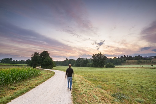 A long exposure shot of a man walking a dirt road towards a beautiful sunset - path to happiness concept