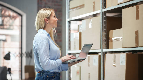 istock Portrait of a Happy Small Warehouse Employee Checking Inventory, Using Laptop Computer. Beautiful Blond Female Smiling in a Storeroom with Parcels and Online Purchased Orders Ready for Shipment. 1478425040