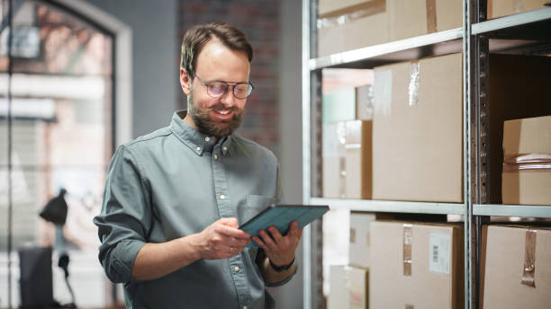 istock Portrait of a Happy Small Warehouse Employee Checking Inventory, Using Tablet. Handsome Man with Moustache Smiling in a Storeroom with Parcels and Online Purchased Orders Ready for Shipment. 1478425126