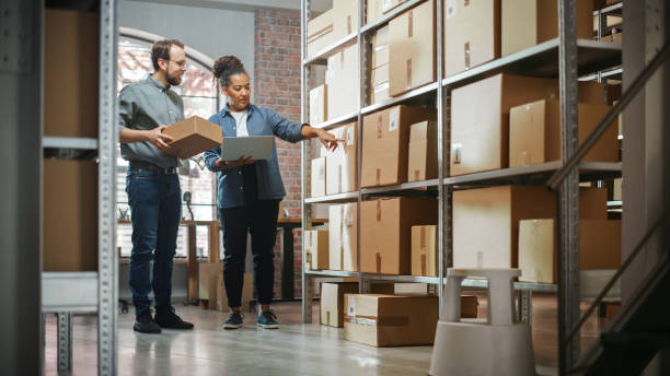 istock Small Business Owner and Employee Checking Stock and Inventory with Laptop Computer in Retail Warehouse full of Shelves with Goods. Working in Logistics, Online Shop Distribution Center. 1478425708
