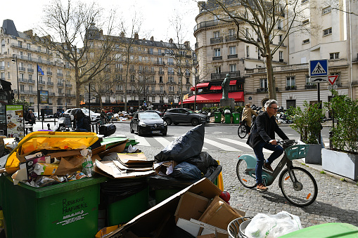 Paris, France-03 31 2023: Pedestrians and cyclists surrounded by piles of waste overflowing from the bins on the boulevard Raspail in the Montparnasse district of Paris, France because of the garbage collectors' strike.