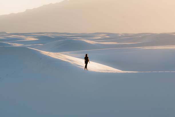 mujer vestida de negro caminando sobre una duna en el parque nacional white sands - white sands national monument fotografías e imágenes de stock