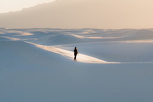 A female in black clothing walking on a dune at White Sands National Park