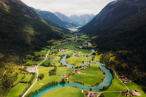 Drone high-angle photo of S-shape glacial river in beautiful green valley with a road surrounded by the mountains in Vestland county, Western Norway