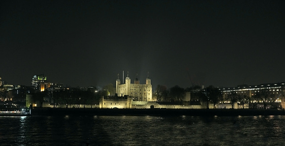 Panoramic view at night of Tower Hill area in London, United Kingdom, including Tower of London, viewed from across the River Thames and illuminated.