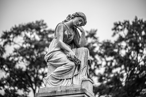 A grayscale view of a sad angel statue in Loudon Park Cemetery in Baltimore, Maryland