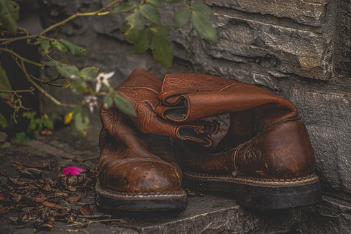 A closeup of pair of worn working or cowboy boots set on stone wall