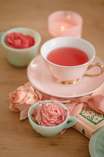 A selective focus shot of cute blue teacups with rosebuds in them, a candle and a diary with a pink ribbon