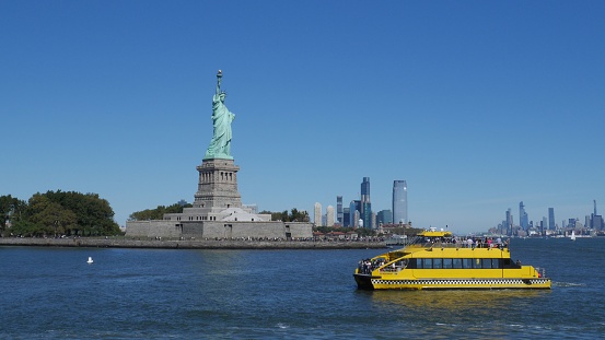 New York, United States – October 01, 2019: A yellow New York Water Taxi in the bay with the Statue of Liberty in the background