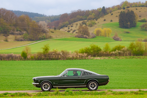 Münsingen, Germany - May 1, 2022: Ford Mustang V8 289 american oldtimer vintage luxury muscle car on a country road near Münsingen, Germany.