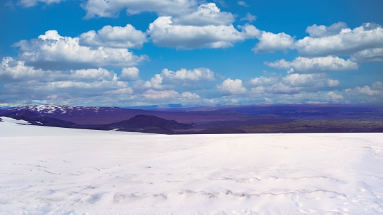 A scenic view of a snow-covered field before the landscape under the partly cloudy sky