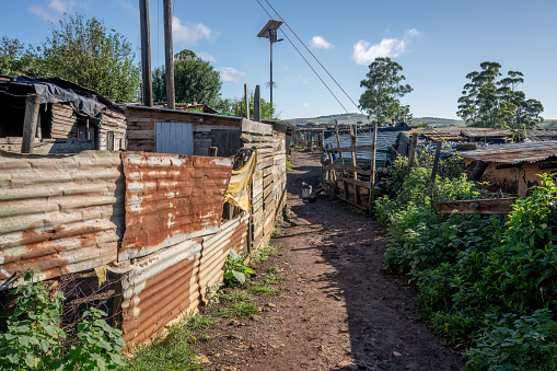 A dirt road passes shacks made from corrugated iron and wood planks in a rural African settlement.