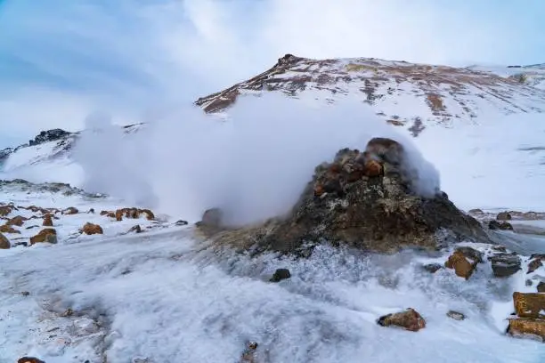 The emission of a fumarole in Hverir Iceland with a snowy mountain in the background