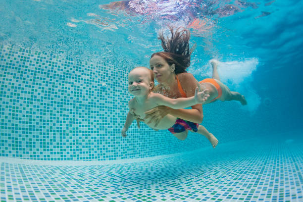 мама, папа с ребенком плавание, ныряние под водой в бассейне - swimming child swimming pool indoors стоковые фото и изображения