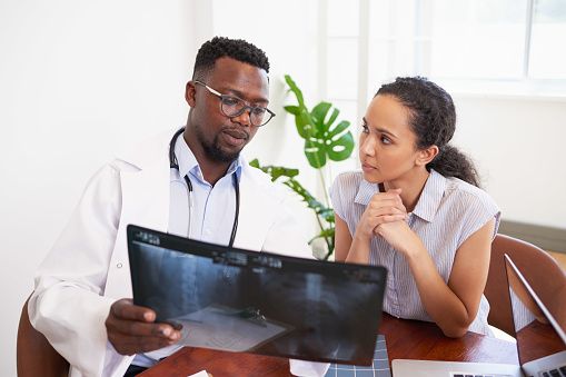 Black male doctor explains x-ray results to young worried patient in doctor office. High quality photo