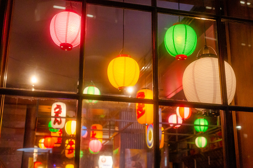 Colorful glowing lanterns illuminated at night in the window of a Japanese restaurant.