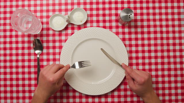 Top view of male hands with cutlery and empty plate on red tablecloth background.
