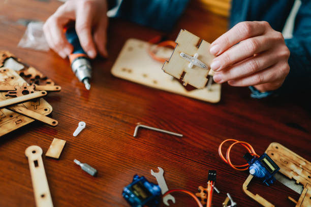 istock Robotic school project: Young student building robot vehicle at artificial intelligence programming class - STEM education concept - Focus on right hand holding wood piece 1478452637