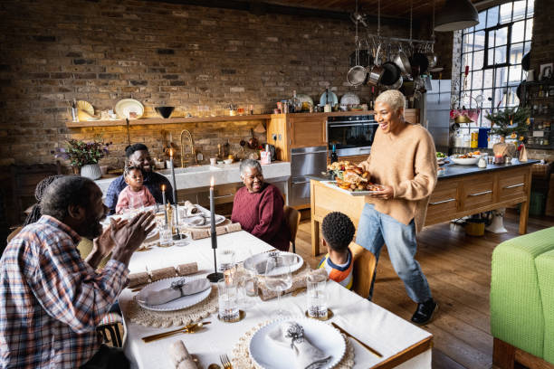 Mother carrying roast turkey to dining table Smiling mid adult black woman bringing Christmas lunch to festive family lunch big family table stock pictures, royalty-free photos & images