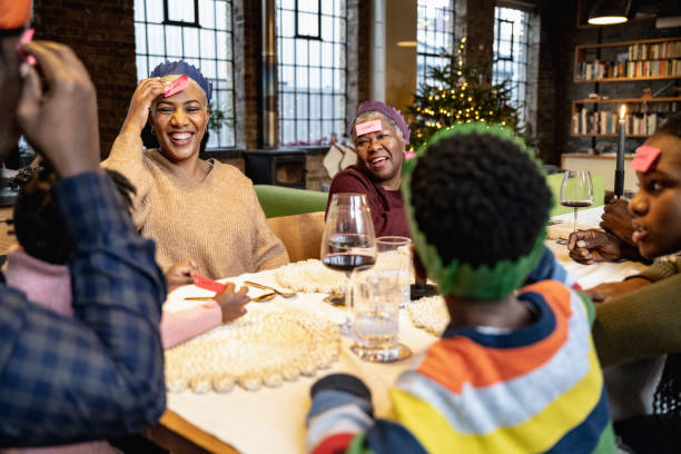 Family play guessing game at Christmas with names of animals on their foreheads Mid adult black female trys to identify what is written on adhesive note on her forehead by asking questions. Fun family parlour game at Christmas. typical average stock pictures, royalty-free photos & images