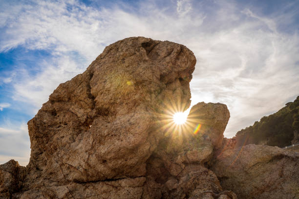 Sunset sun appearing between some rocks on the beach.