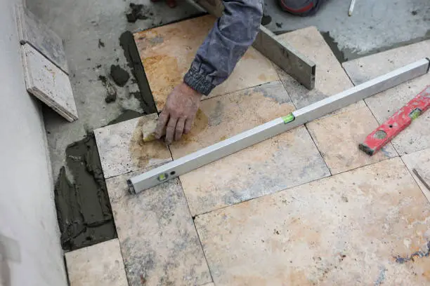 Worker lying down travertine stone tiles on a patio.