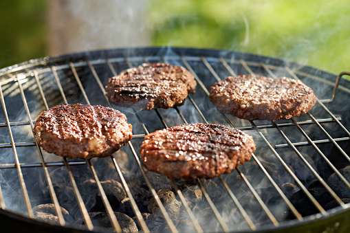 hamburger patties being grilled on charcoal kettle grill