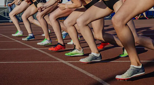 legs female athletes in running spikes shoes on starting line of middle distance race, olympic summer sports