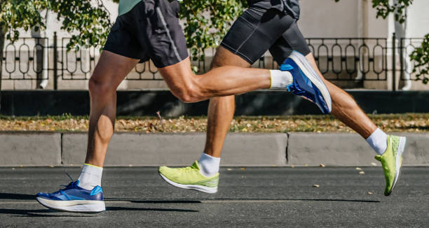 beine zwei männliche läufer laufen stadtmarathon, athleten joggen auf asphaltstraßen, sommersportspiele - scoring run stock-fotos und bilder