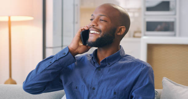 istock Happy, speaking and a black man on a phone call on the sofa for communication, chat and relaxation. Smile, looking and an African guy talking on a mobile while sitting on the couch for conversation 1478468825