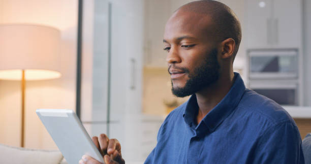 istock Internet, tablet and remote work, black man in living room reading email, social media or networking online for freelance job. Technology, communication and happy freelancer on sofa on web search. 1478471012