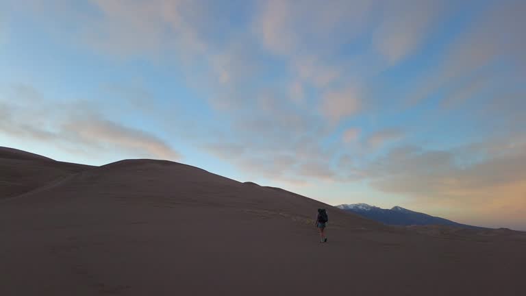 Woman Backpacks Across Sand Dunes
