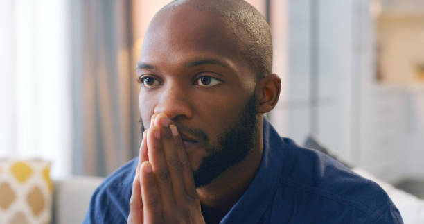 istock Man, living room and prayer hands for stress, vision and problem in life with mindset for solution. African male, lounge and remember with regret, mistake or fail in house, silent and quiet thinking 1478475207
