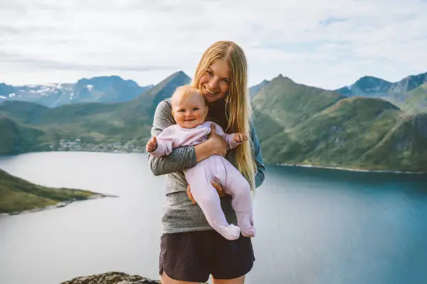 Photo of Mother with infant baby outdoor family lifestyle travel together in Norway summer vacations woman with child Mothers day holiday