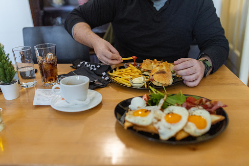 One man is having a brunch of eggs, bacon, toast, and a tasty sandwich with fries, enjoyed with a hot cup of coffee on a cozy morning.