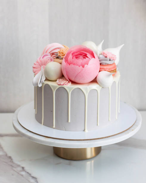 Beautiful and elegant grey cake decorated with melted white chocolate, macaroons, pink peony flower, cake pops and candies on marble cakestand