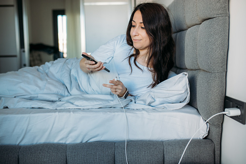 Woman inserting charging cable in smartphone when lying in bed