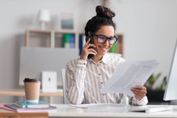 istock Corporate communication concept. Happy female manager reading financial documents and talking on cellphone 1478504503