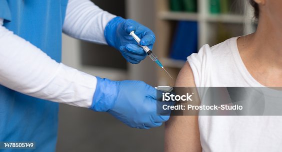 istock Hands of doctor in protective gloves make injection with syringe of old caucasian female patient in clinic 1478505149